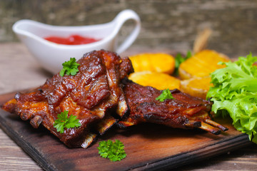 Appetizing rosy and barbecued lamb ribs seasoned with a barbecue sauce and served with fresh herbs and potatoes on an old rustic wooden chopping board