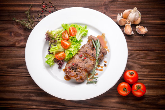 Beef steak with vegetables and seasoning on wooden background