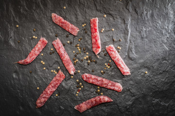 Dry smoked pork sausage lying on the stone slab. Multicolored pepper.