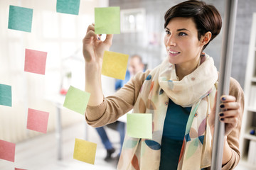 Woman make scheme on sticky notes on glass board