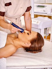 Obraz na płótnie Canvas Head of young woman lying with closed eyes receiving electric ultrusound facial massage at beauty salon. 