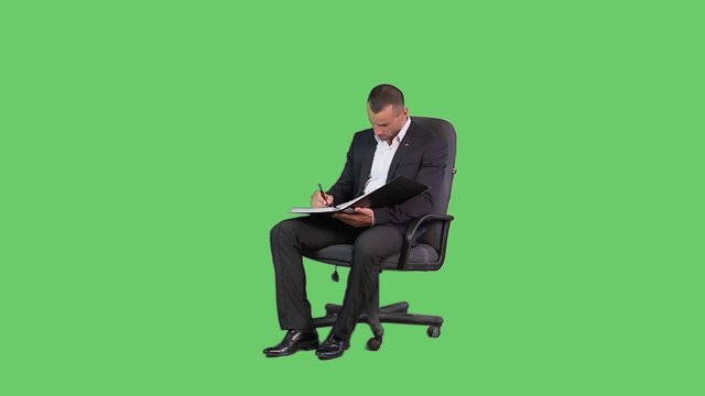 A man in an armchair in a jacket and a green background