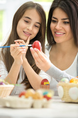 Smiling mom painting Easter eggs with daughter