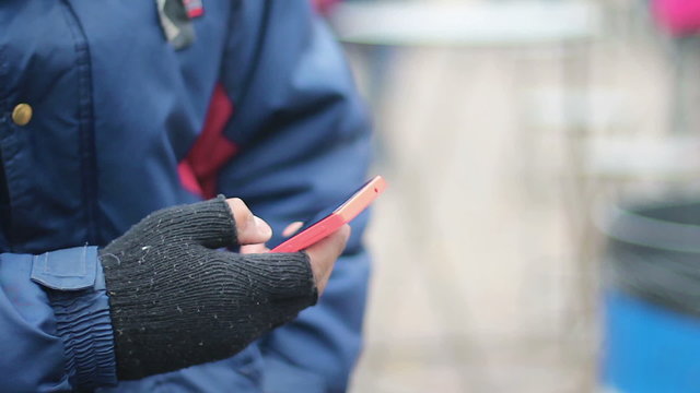 Male hand in old fingerless gloves using touch phone, poor man texting message