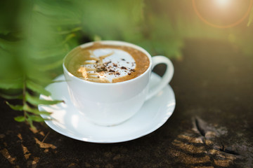 Cup of coffee cappuccino art on wood floor with green leave fram