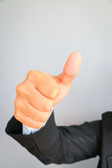 Business man in suit with red tie showing thumbs up sign on gray background.