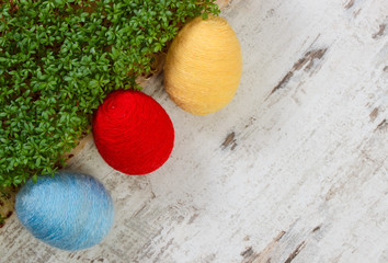 Easter eggs wrapped woolen string and green cress on wooden background, copy space for text, decoration for Easter