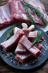 Raw sliced pork ribs with seasonings on a basalt plate, close-up
