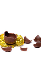 Easter egg broken into small pieces half the egg is on its gold foil wrapping.