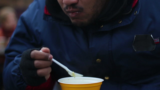 Hungry pauper eating food donated by volunteers, charity event for poor people