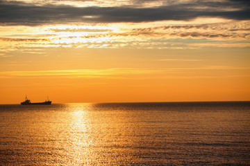 Naklejka na ściany i meble Cargo ship sailing on sunrise near the beach