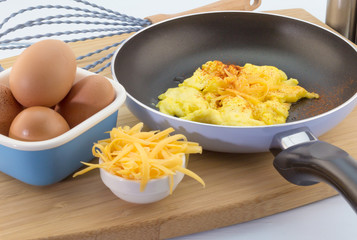 Scrambled egg in pan sprinkled with cayenne pepper and cheddar c