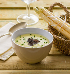 Asparagus soup on a wooden table with fresh asparagus in a basket