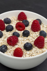 Rolled oats (oat flakes) in a bowl with raspberries, blueberries