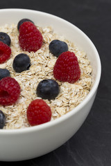Rolled oats (oat flakes) in a bowl with raspberries, blueberries