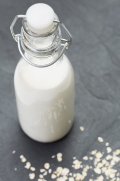 Bottle of milk with rolled oats (oat flakes) on a black slate