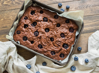 Chocolate brownie with blueberries in the baking pan on a wooden table