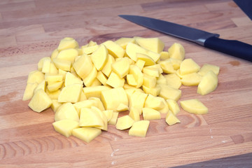 Preparing food. Big pile of sliced potatoes on kitchen cutting brown wooden board. Horizontal photo closeup