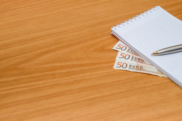empty notepad with euro banknote, pen on table