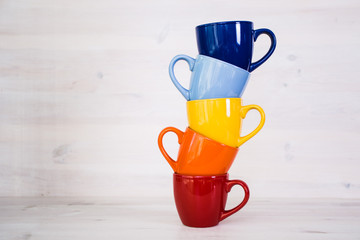 a stack of colorful coffee cups on a white wooden background - 104720507