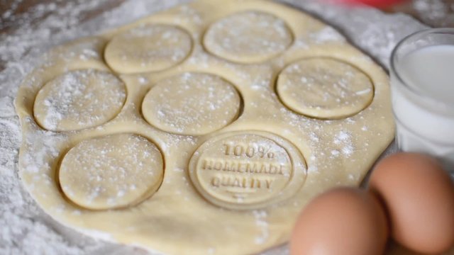 Locked down close up - young woman's hand stamping rolled out dough with a wooden stamp. The imprint on the dough says "100% homemade quality"