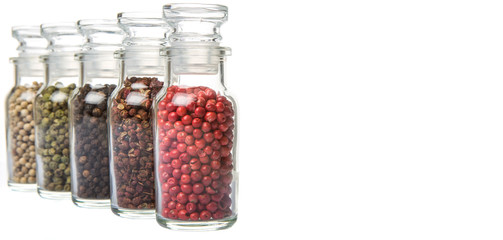 Szechuan peppercorns, green peppercorns, white peppercorns, black peppercorns and pink peppercorns in glass vial over white background