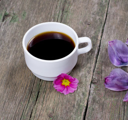 the cup of coffee decorated with a pink flower and lilac petals