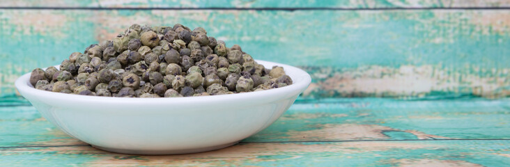 Dried green peppercorn in white bowl over wooden background