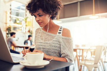 Attractive young woman with earphones using laptop at cafe