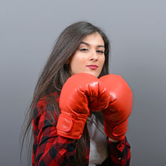 Portrait of young woman posing with boxing gloves against gray b