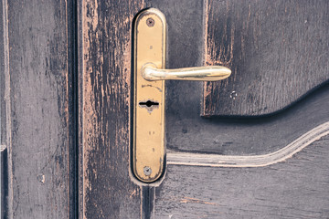 Door handle of gold color with an old wooden door