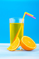orange juice in a glass with colored straws and orange slices on a blue background