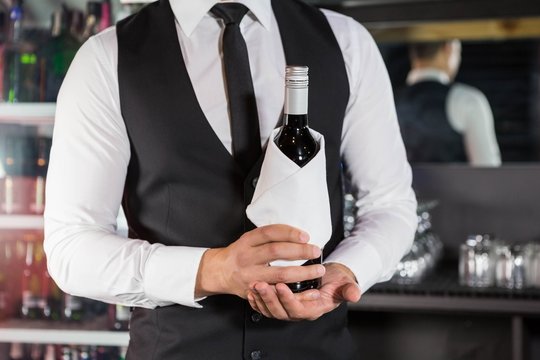 Mid section of bartender holding a wine bottle
