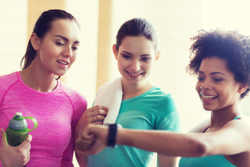 happy women showing time on wrist watch in gym