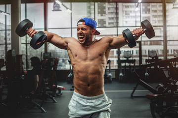 Fototapeta na wymiar Handsome man lifting dumbbells at gym. Free weights.