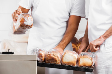 Midsection Of Baker's With Packed Bread Loaves In Bakery