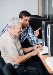 Fototapeta na wymiar Tutor Helping Senior Man In Using Computer