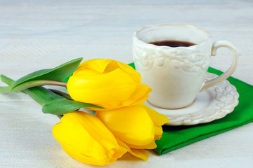 yellow tulips with a Cup of coffee lying on a napkin on white wooden table