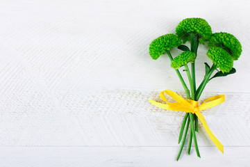 fragrant green chrysanthemums  with yellow ribbon on white wooden table
