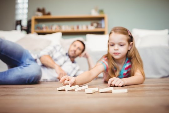 Girl arranging domino while father lying on hardwood floor