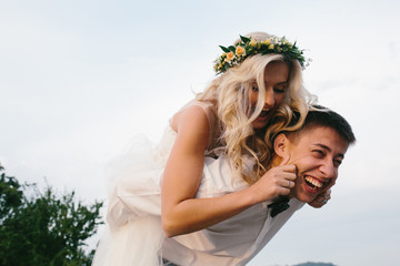 groom carries bride on his back outdoors