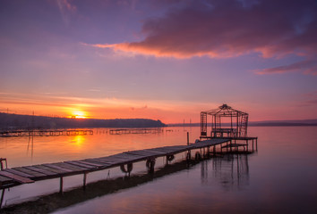 Fototapeta na wymiar Sunset on the bay with old wooden bridge pier with gazebo