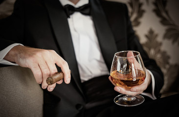 Gentleman holding glass of cognac and cigar