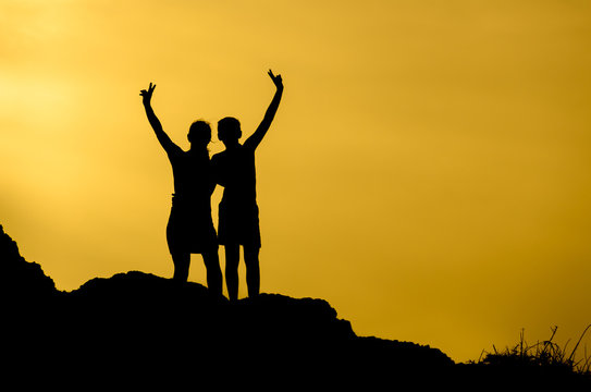 Silhouette of a couple making the sign of victory on top of a hill