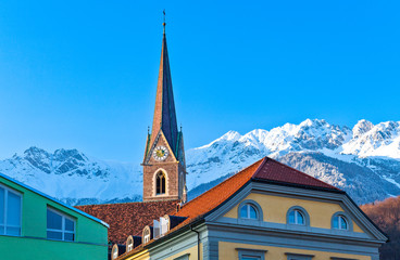 Fototapeta na wymiar Austria, Innsbruck, view of the snowy mountains fom the Inn river bank with old houses and bell tower in the foreground