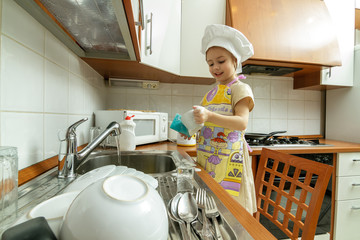 Little girl in white chef hat is washing dishes in the kitchen.
