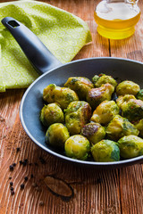 Fried brussels sprouts in a pan on the wooden background.