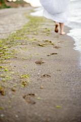 The girl in a white dress running down the beach, leaving footprints in the sand