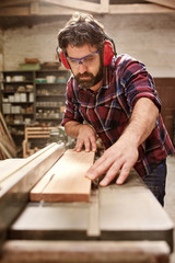 Carpenter wearing protective gear cutting a plank of wood
