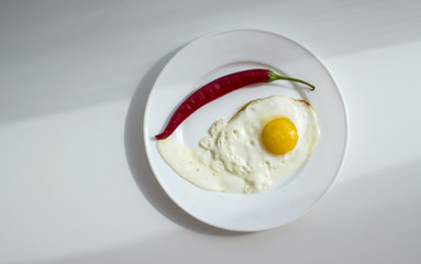 Fried eggs on white plate with red hot pepper on light background